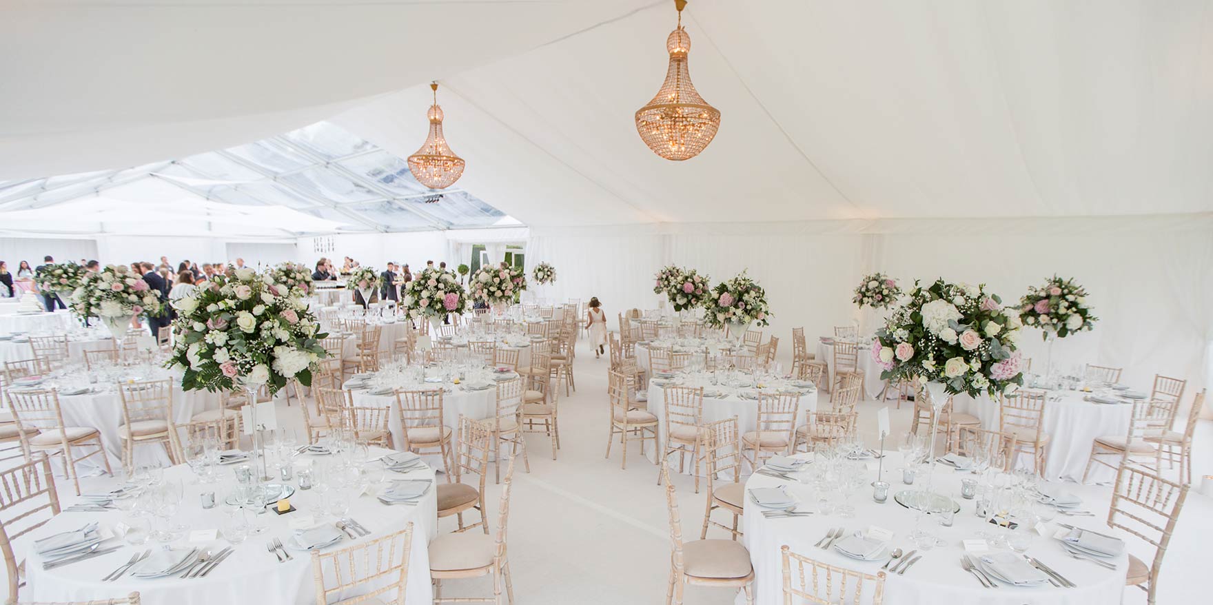 Wedding with white linings for marquee hire with copper effect chandeliers and large floral arrangements to circular table centres