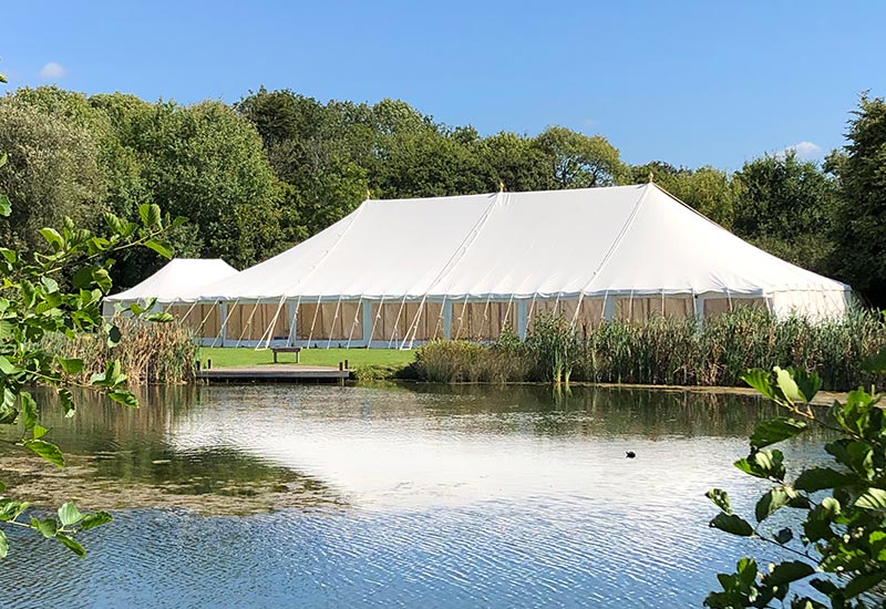 Duncton Mill Fishery wedding venue with large marquee beside fishing pond surrounded by reeds