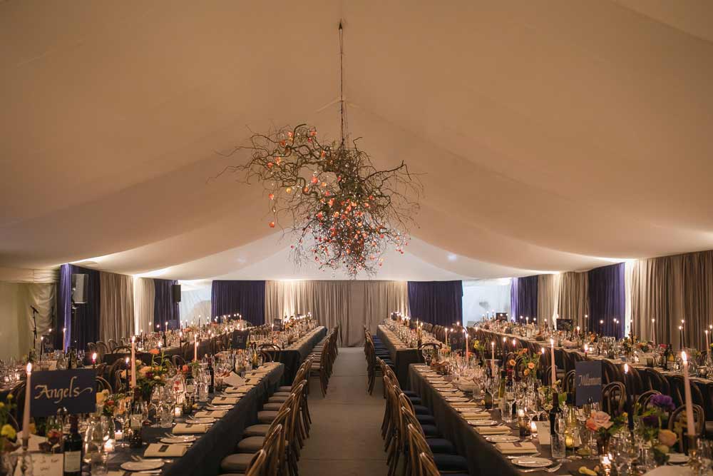 Dining marquee with velvet wall drapes, long tables and flat ivory linings with nature inspired ornament to ceiling