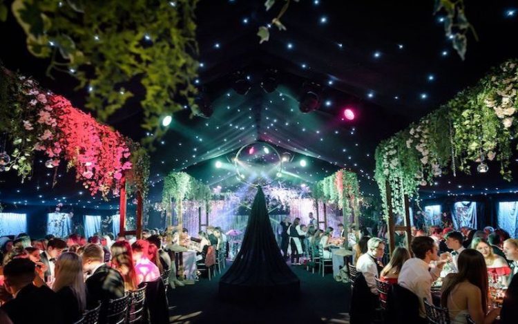 Dark starlit party marquee with floral arrangements and green and red lighting and ring suspended from ceiling