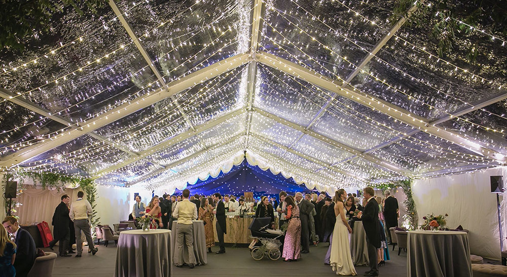 Reception marquee with starlight reveal combined with a clear roof and guests mingling around hired bar